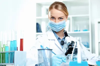 молодая девушка-врач в медицинской маске держит много масок в руках.  медсестра позирует на синем фоне Стоковое Фото - изображение насчитывающей  пакостно, чисто: 218949594