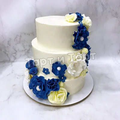 Лаконичный белый свадебный торт, украшенный цветами и ягодами из мастики.  Торт стоит на белой подставлке на белом деревянном фоне. Вид спереди Stock  Photo | Adobe Stock